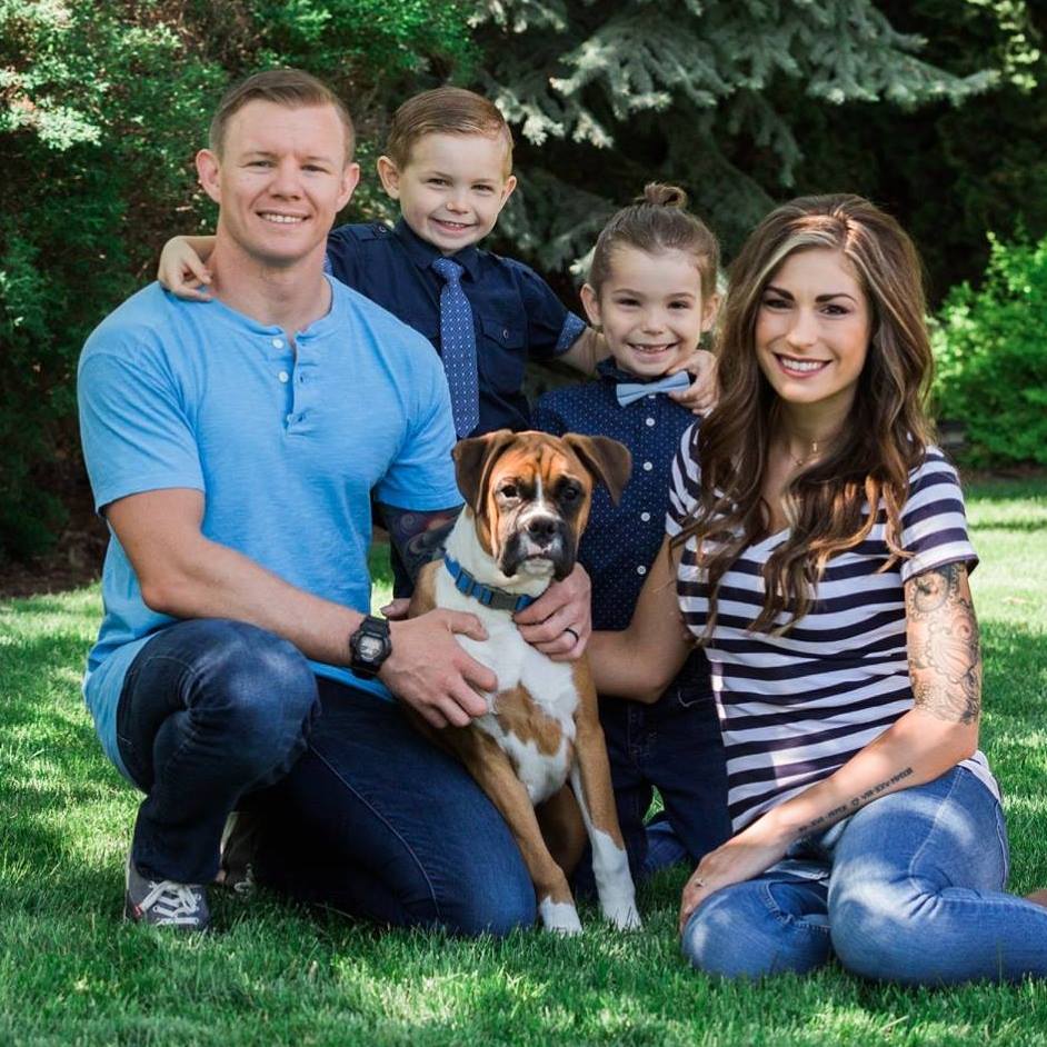 Danielle, her husband, her two sons, and a boxer dog sitting on a lawn and smiling for the camera