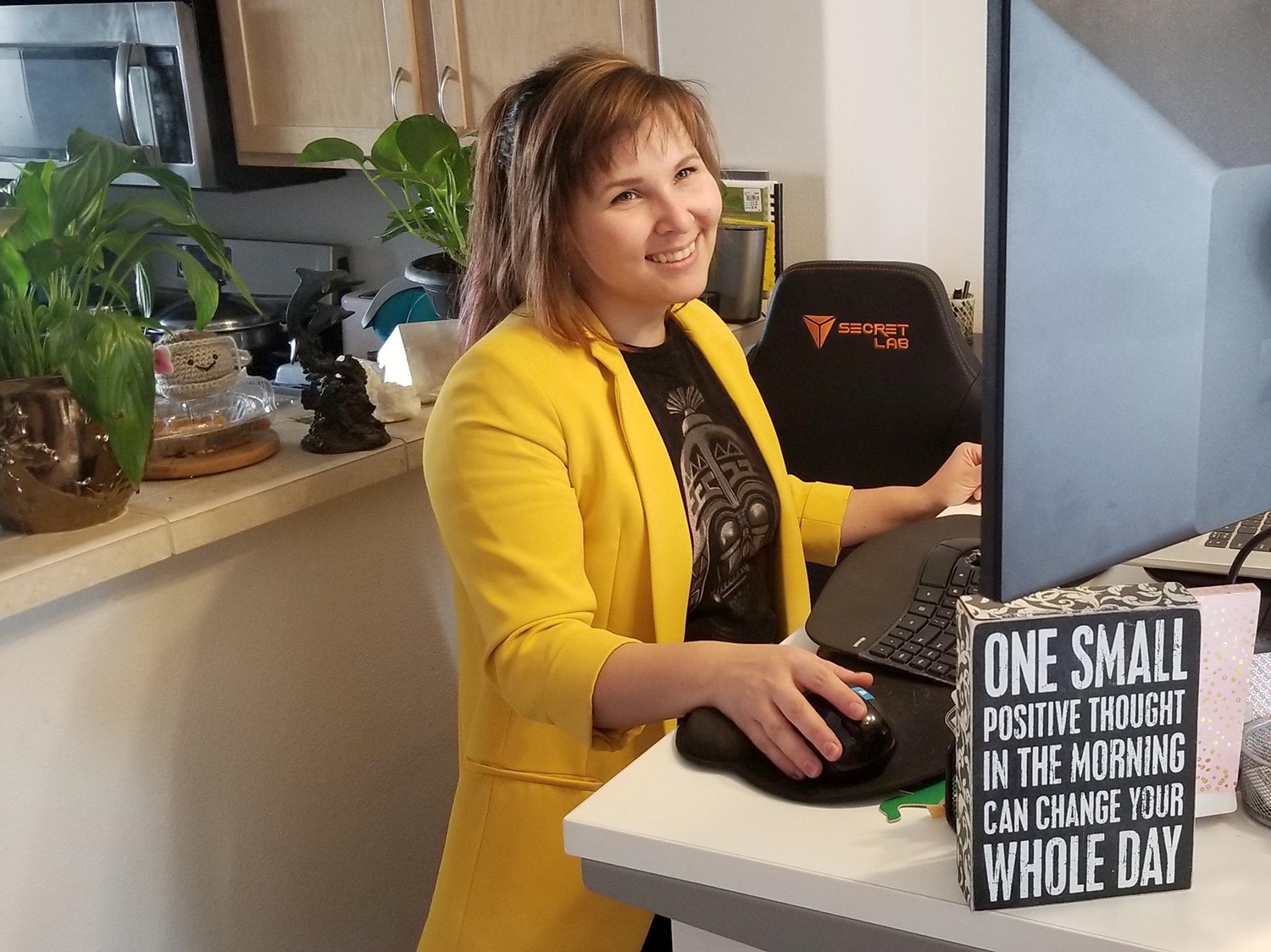 A woman wearing a yellow blazer, smiling while working at a computer in her home
